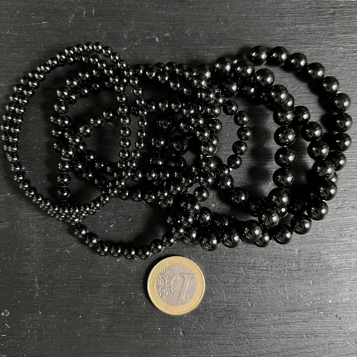 Mehrere schwarze Turmalin Armbänder mit hochglanzpolierten Kugelperlen 3–4mm, tiefschwarz ohne Einschlüsse, neben 1-Euro-Münze | Happy Minerals