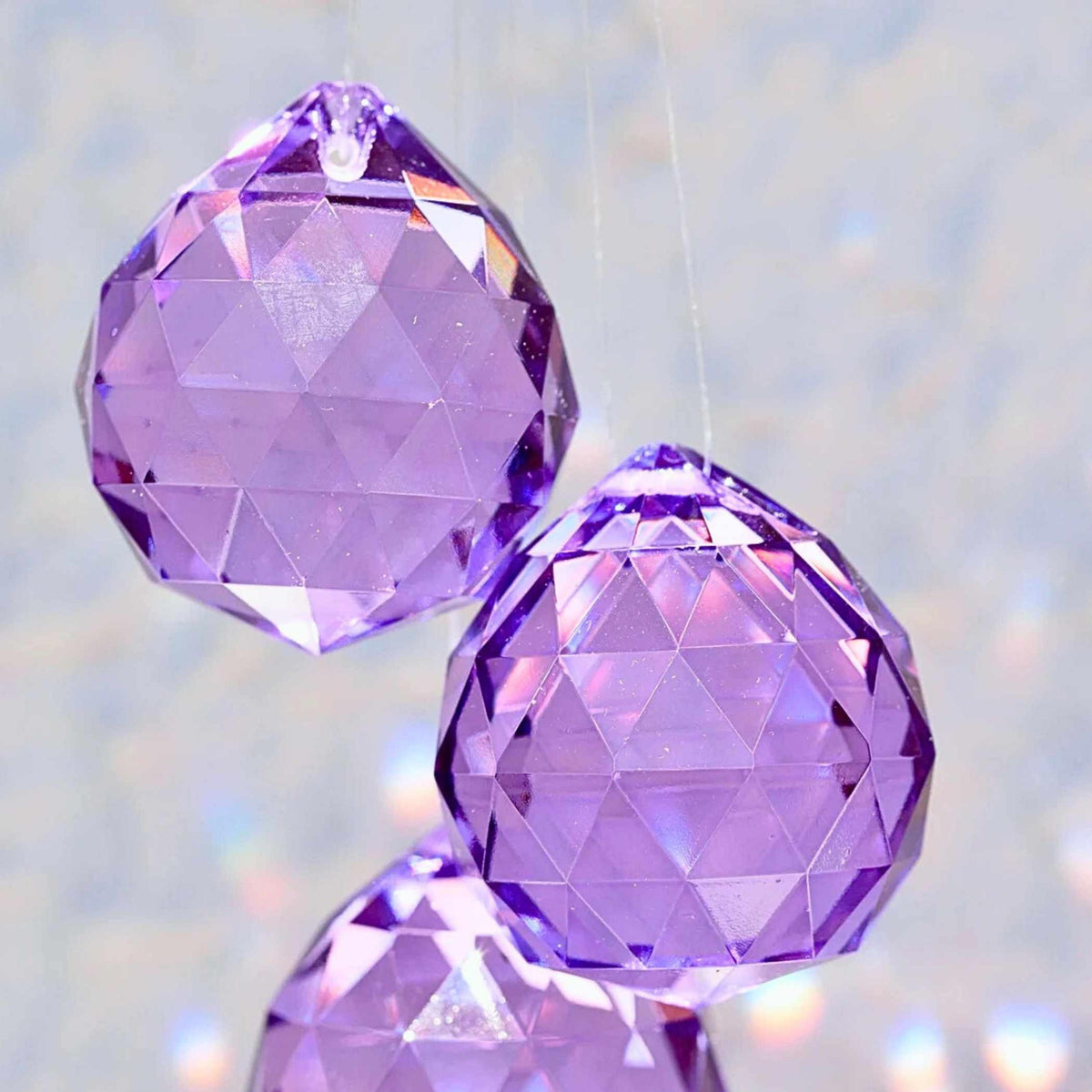 Lila Kristall-Sonnenfänger hängt im Fenster und wirft violette Lichtreflexe | Happy Minerals
