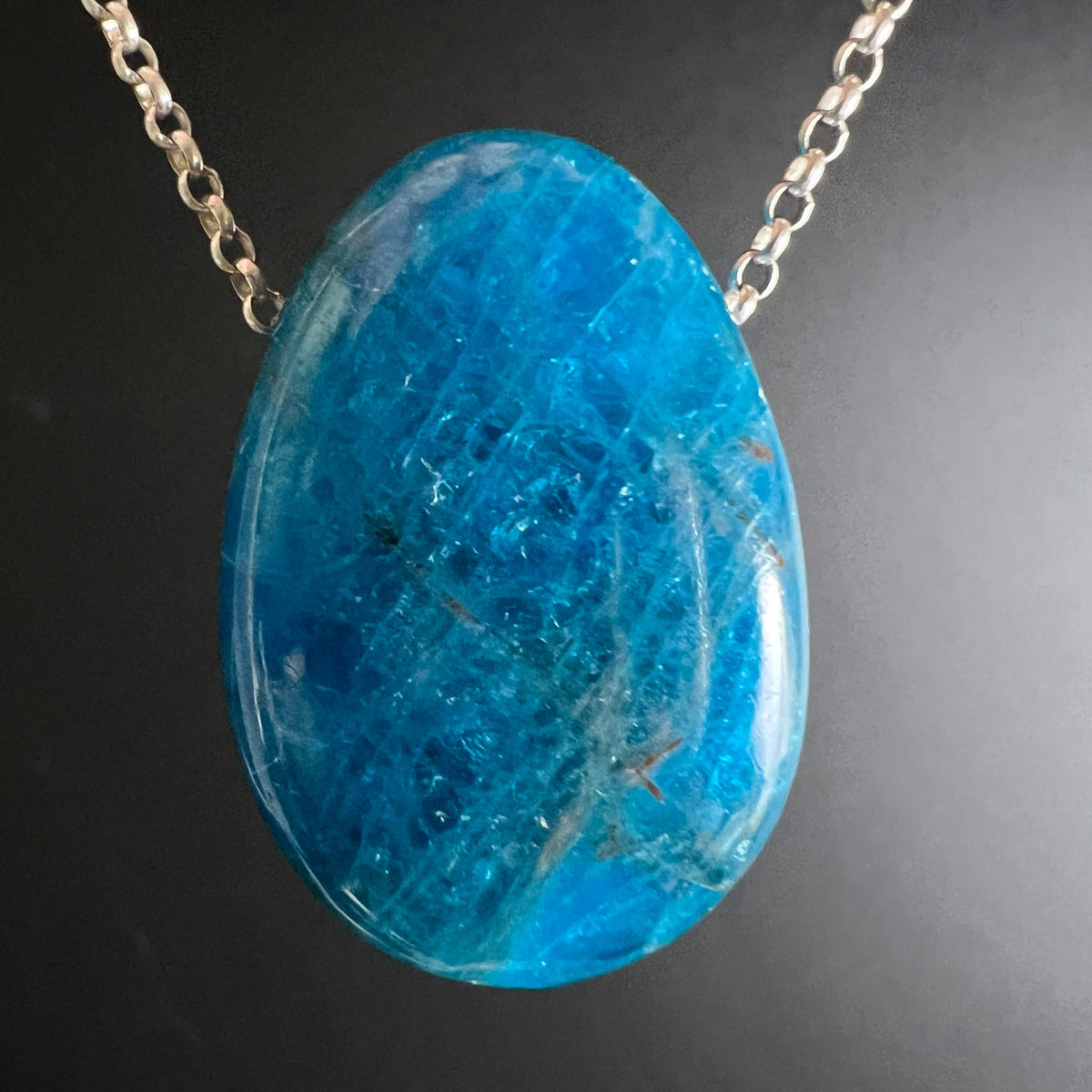 Blauer Apatit Anhänger | auf silberner Kette | leuchtend blau | dunkler Hintergrund | Happy Minerals