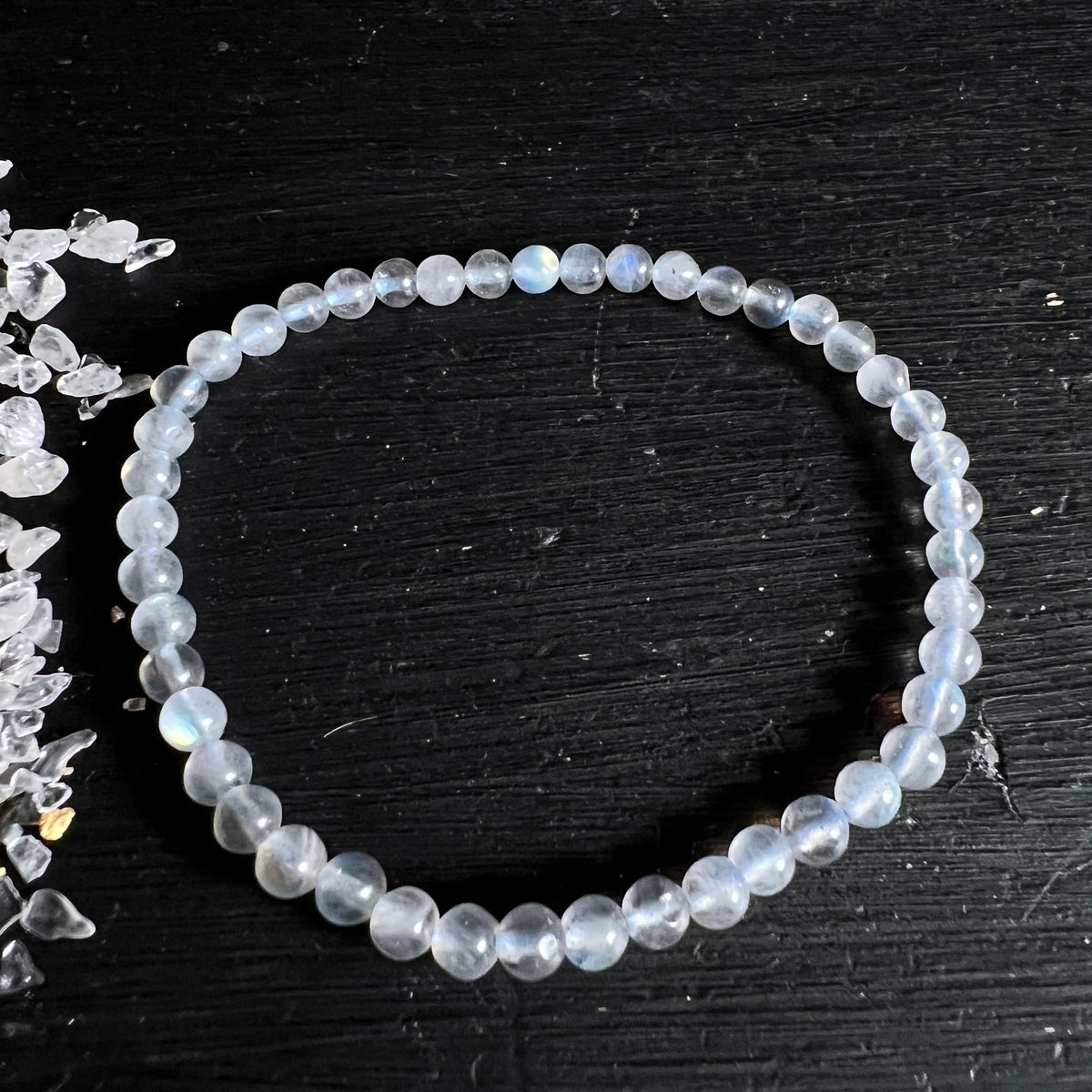 Armband aus kleinen runden, milchig-transparenten Perlen mit bläulichem Schimmer, 4mm, auf schwarzem Holz | Happy Minerals