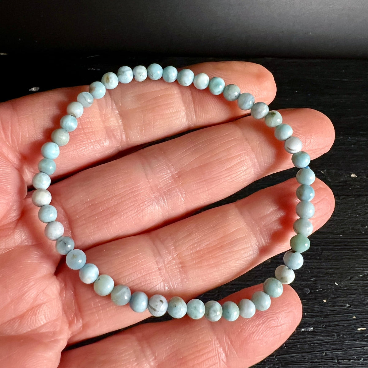 Larimar Armband aus kleinen polierten Perlen in hellblau-weissem Marmormuster, an Hand gehalten | Happy Minerals