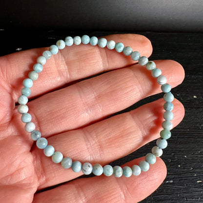 Larimar Armband aus kleinen polierten Perlen in hellblau-weissem Marmormuster, an Hand gehalten | Happy Minerals