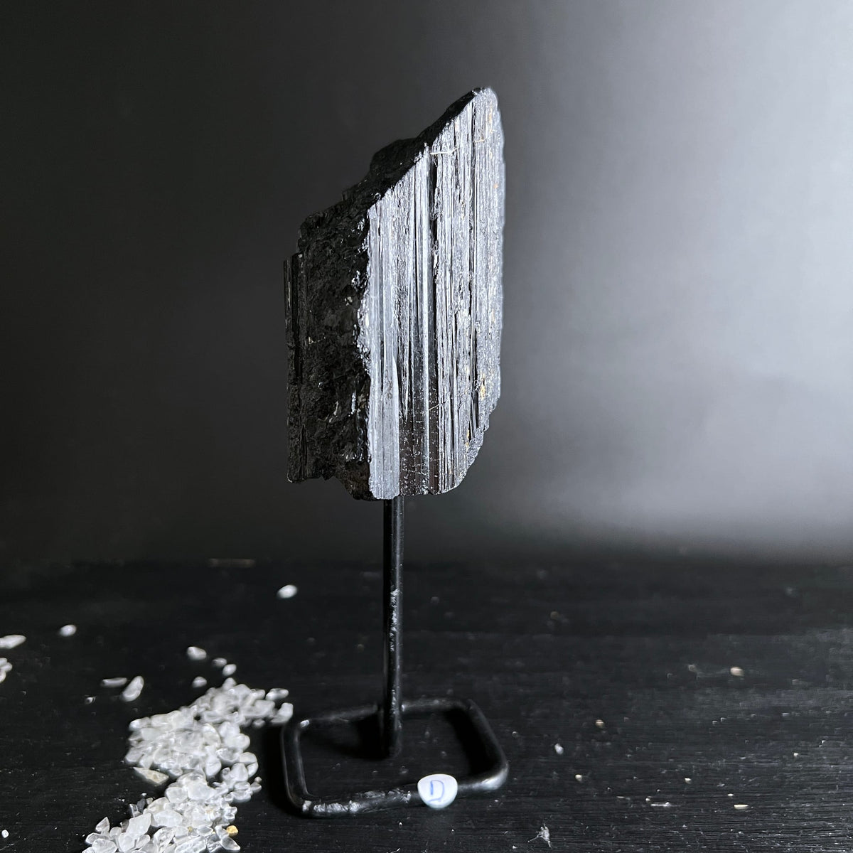 Schwarzer Turmalin Rohstein mit silbrig-grauen Faserstreifen und rauer Bruchkante, auf Metallständer | Happy Minerals