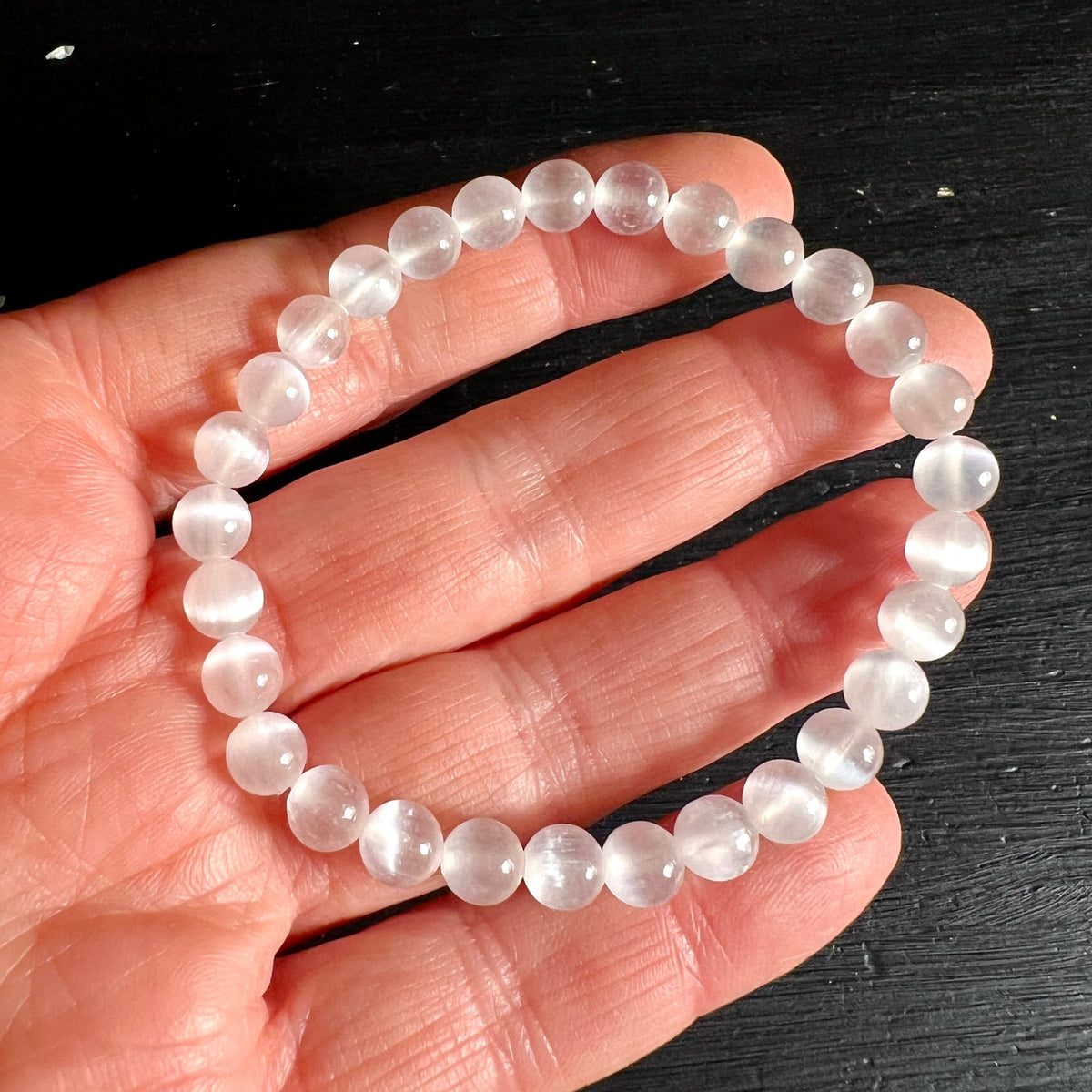 Selenit Armband mit milchig-transluzenten Perlen, zartes Cat's-Eye-Lichtband sichtbar, an Hand gehalten | Happy Minerals