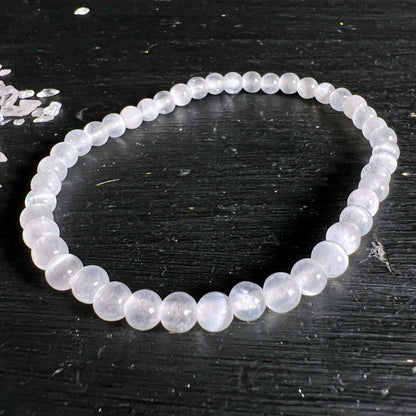 Selenit Armband aus milchig-weissen, transluzenten Perlen mit seidigem Glanz auf dunklem Holz | Happy Minerals