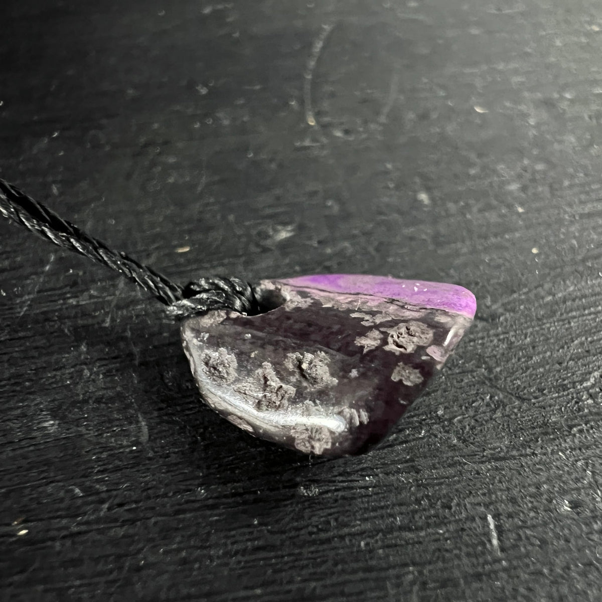 Sugilith Anhaenger, dunkles Violett-Grau mit rosa Zone, raue Textur, an schwarzer Kordel | Happy Minerals