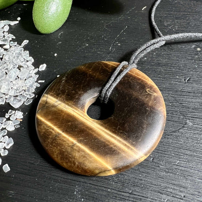 Matter Tigerauge Donut 50mm mit samtiger Oberflaeche neben Bergkristall